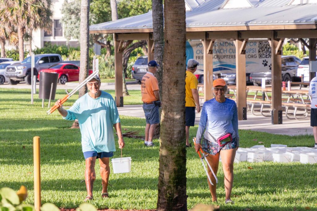 Two participants walking through the park carrying beach cleanup supplies.