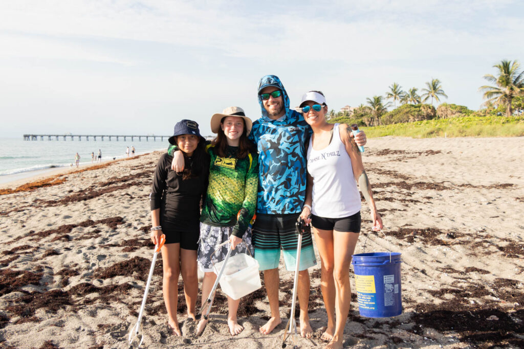 Group of volunteers posing together on the beach with cleanup buckets.