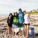 Group of volunteers posing together on the beach with cleanup buckets.