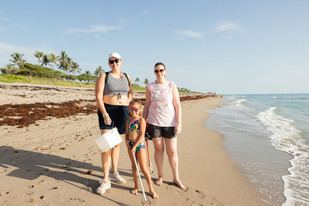 Three volunteers posing together on the beach after a cleanup.