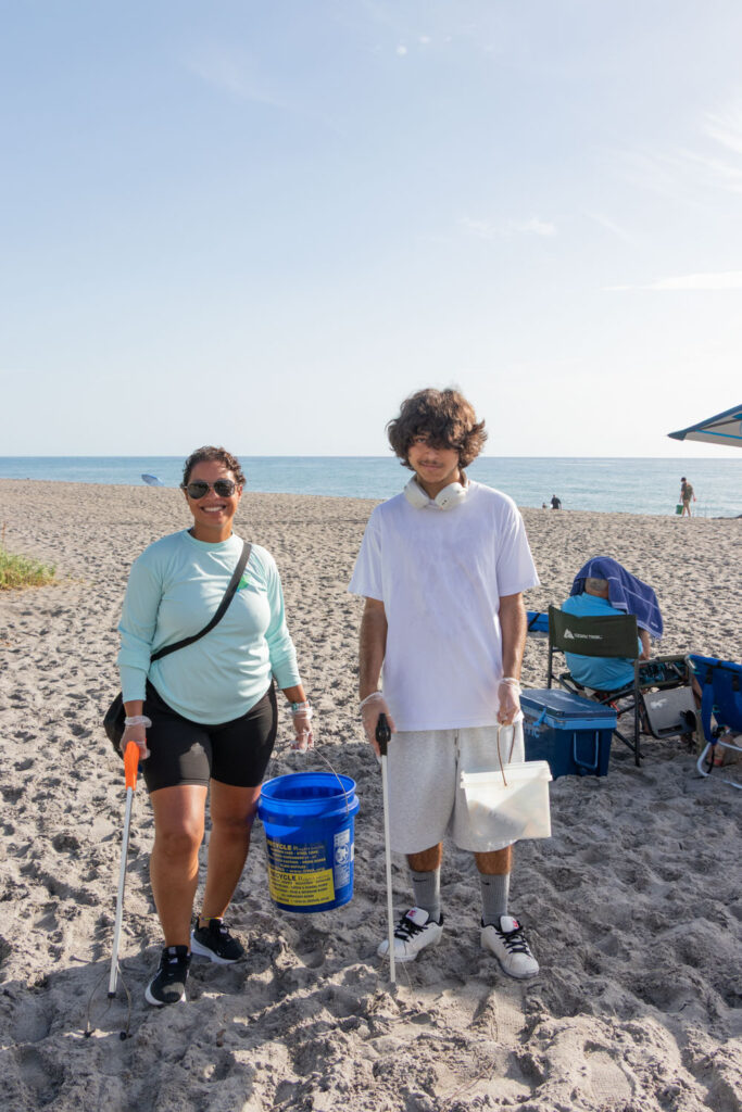 Two volunteers posing together with cleanup buckets on the beach.
