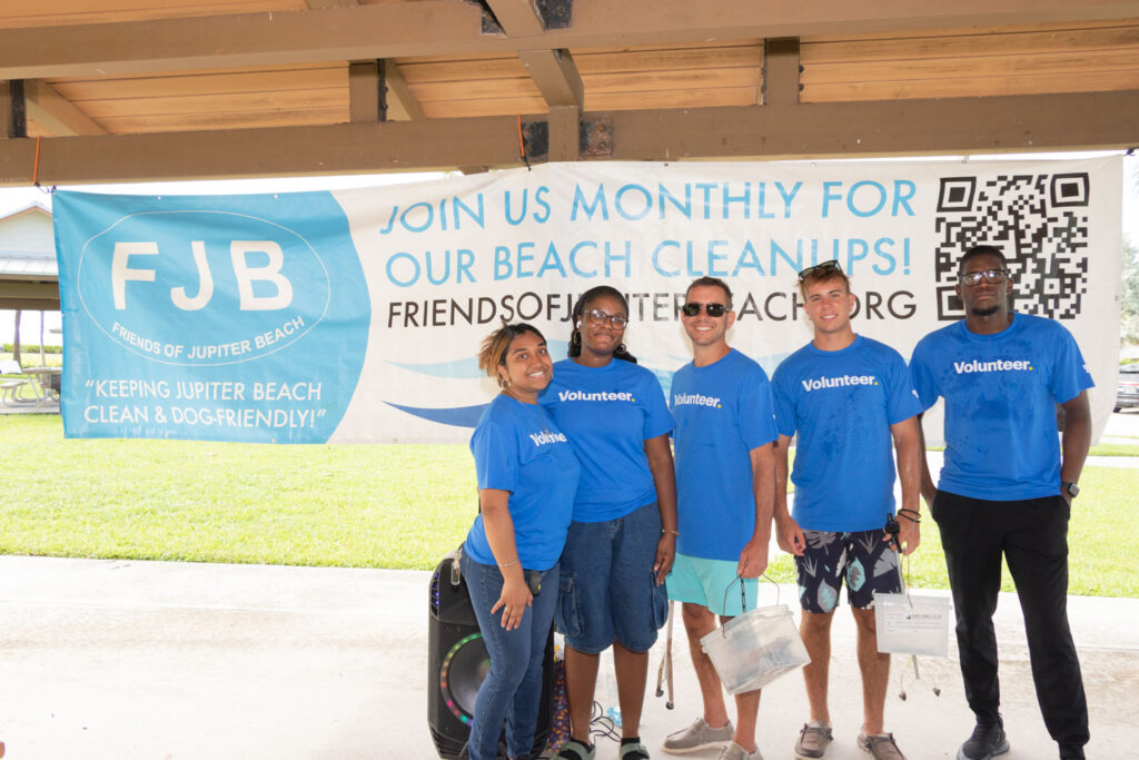 Volunteers standing together beneath the beach cleanup event banner.