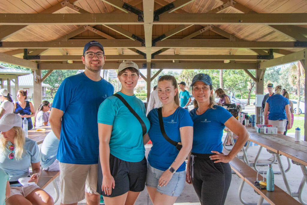 Group of four volunteers posed and smiling under Anita Lankler Pavilion in Juno Beach.