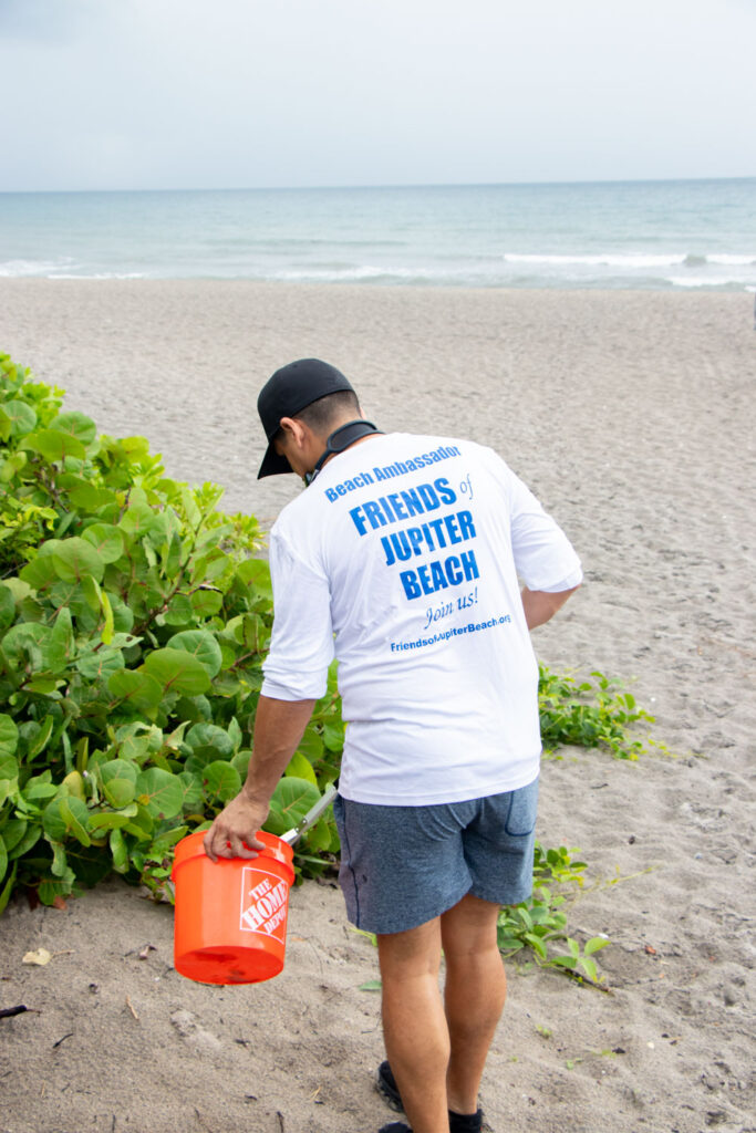 Friends of Jupiter Beach volunteer picking up trash using collection equipment.