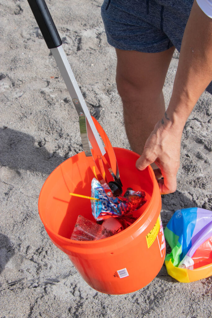 Trash pickers placing juice box inside orange trash bucket.