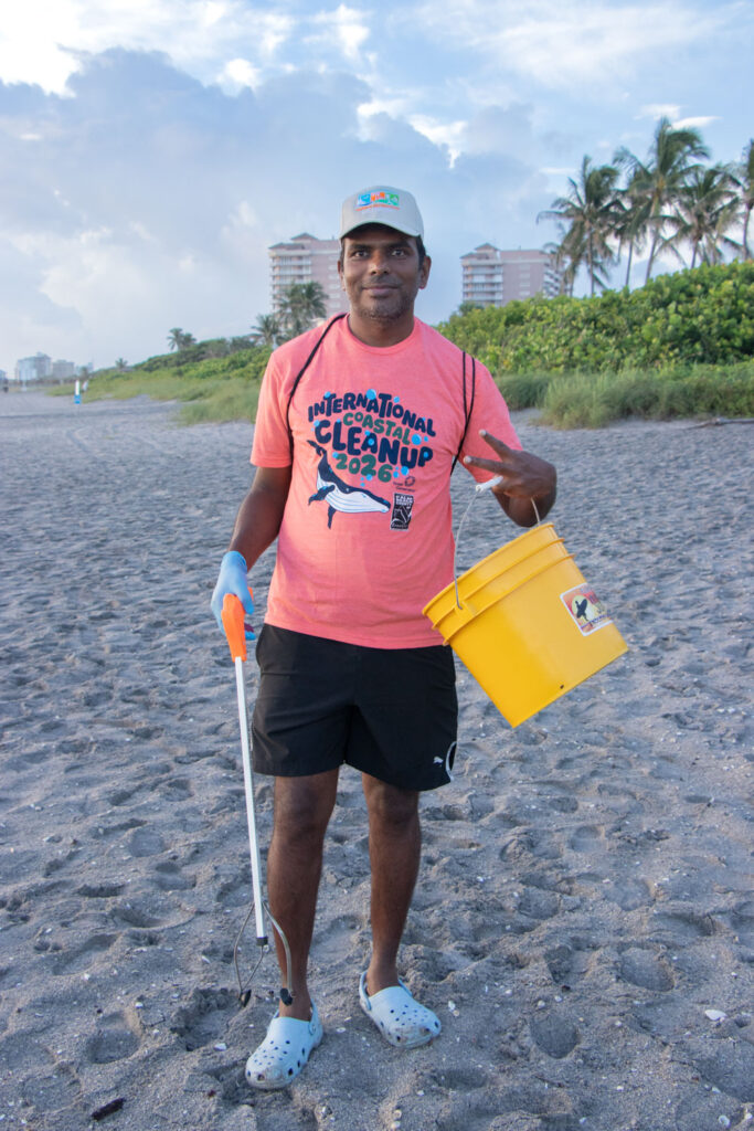 International Coastal Cleanup volunteer with trash buckets and pickers standing on Jupiter Beach.