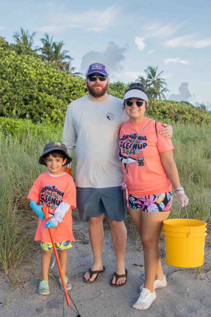 Three International Coastal Cleanup volunteers with trash buckets and pickers standing on Jupiter Beach.