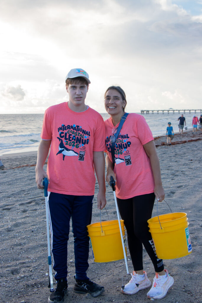 Two International Coastal Cleanup volunteers with trash buckets and pickers standing on Jupiter Beach.