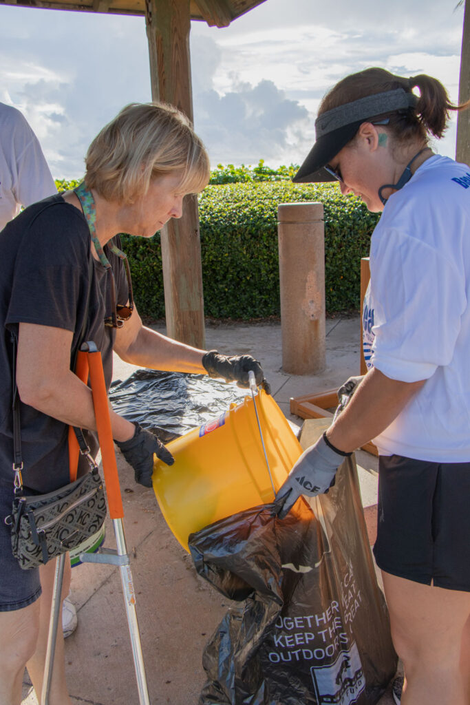 International Coastal Cleanup volunteer emptying their trash bucket into a trash bag held by another volunteer.