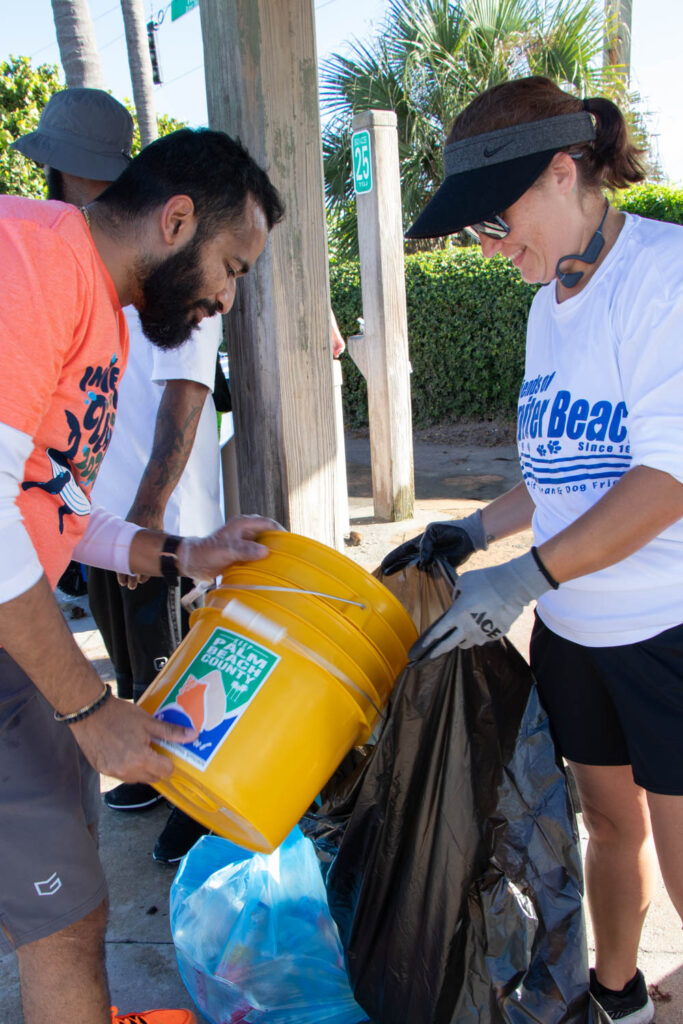 International Coastal Cleanup volunteer emptying their trash bucket into a trash bag held by another volunteer.