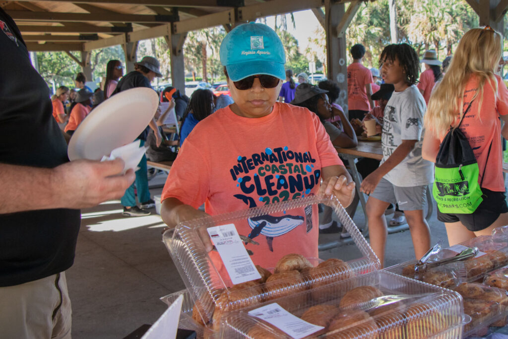 International Coastal Cleanup volunteer grabbing a croissant with tongs under a beach pavilion.