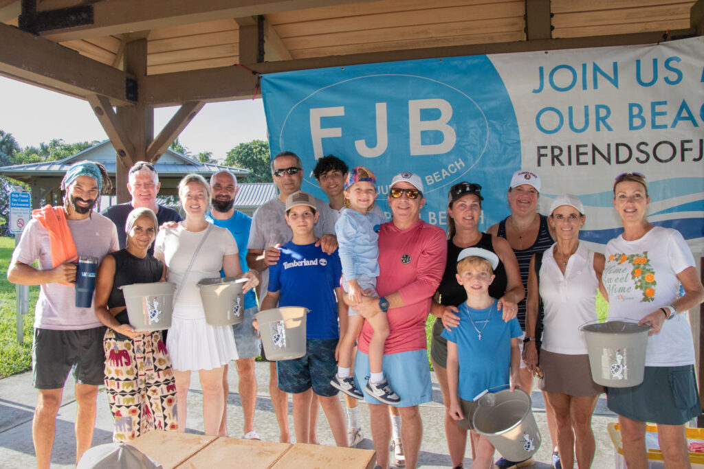 Large group of Friends of Jupiter Beach volunteers smiling and holding trash pickup buckets.