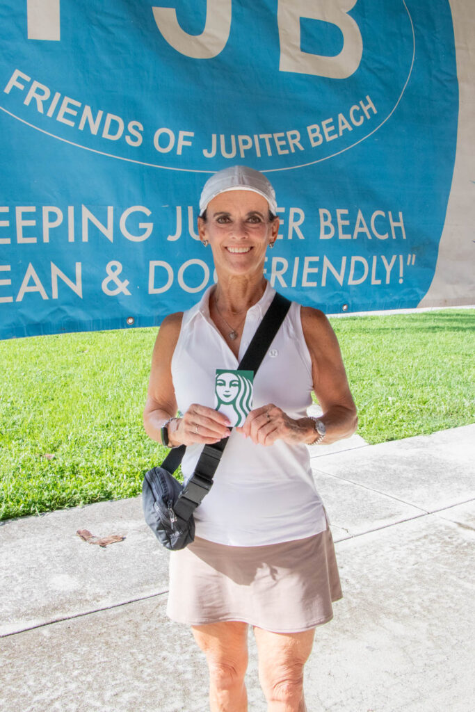 Young female volunteer holding up a Starbucks Coffee gift card and smiling.