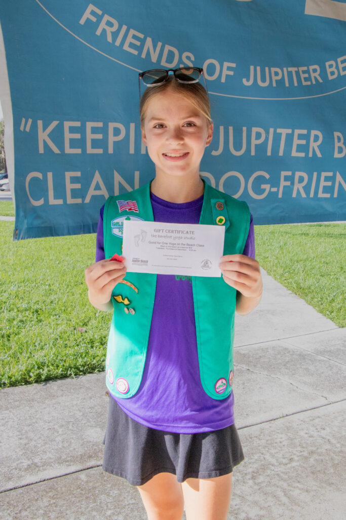 Young volunteer in a green Girl Scouts vest holding up a Gift Certificate.