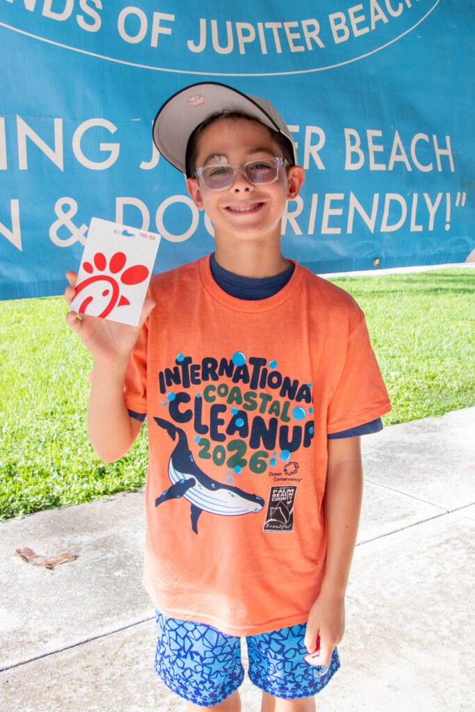 Young volunteer in orange International Coastal Cleanup T-shirt smiling and holding up a Chick-Fil-A gift card.