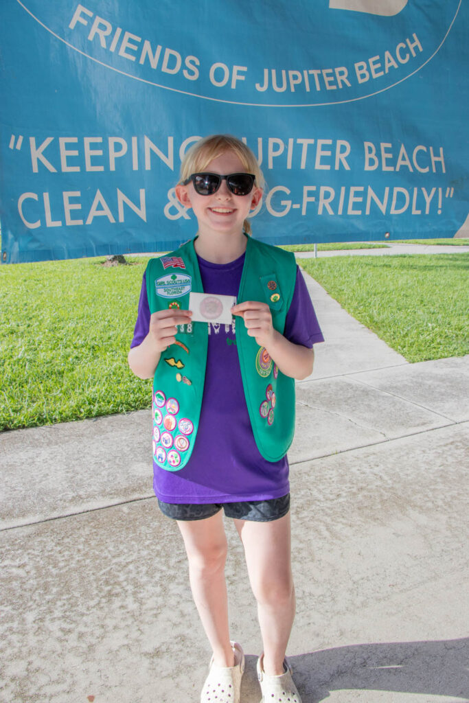 Young volunteer in Girl Scout vest holding up a gift card.