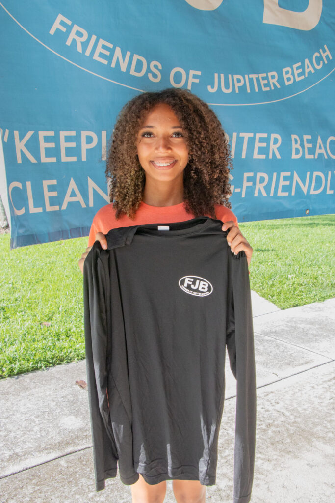 Young volunteer holding up Friends of Jupiter Beach long sleeve grey T-shirt.