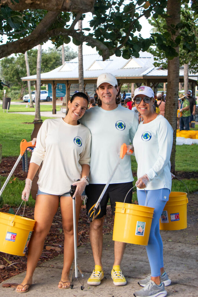 Beach cleanup volunteers holding bucket and cleanup supplies and smiling.
