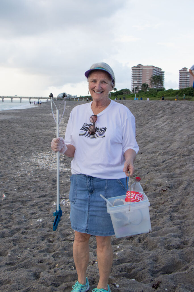 Beach cleanup volunteer holding bucket and cleanup supplies.