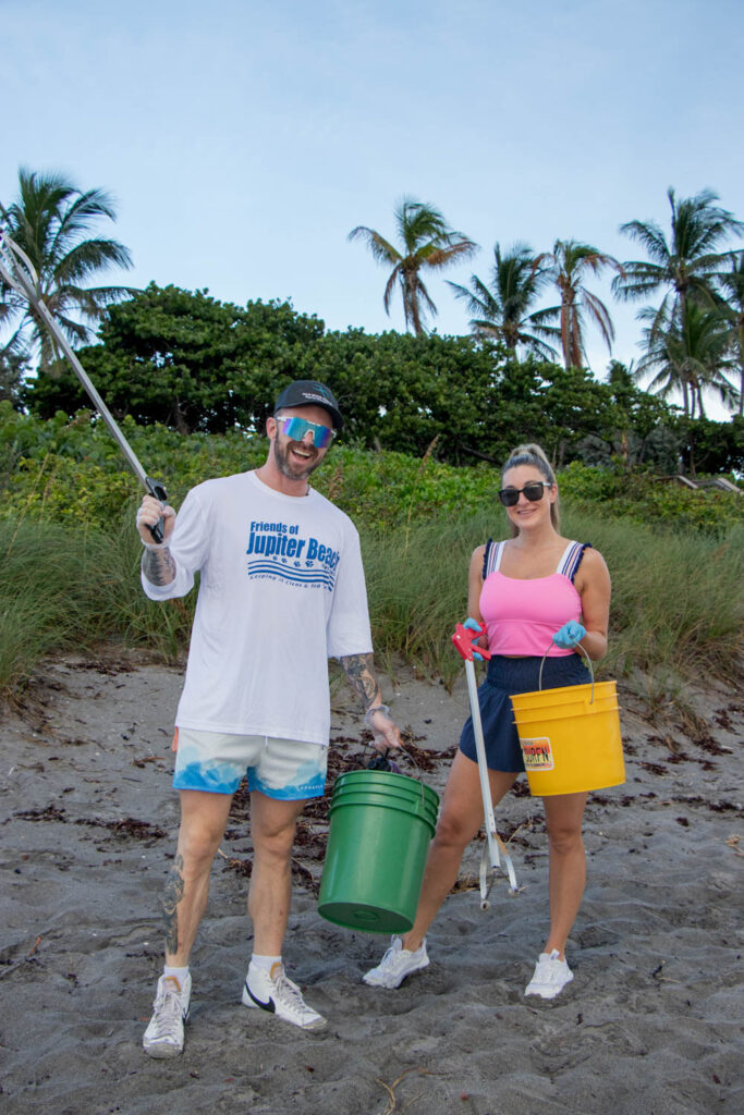 A man and women posing on the beach with cleanup supplies.