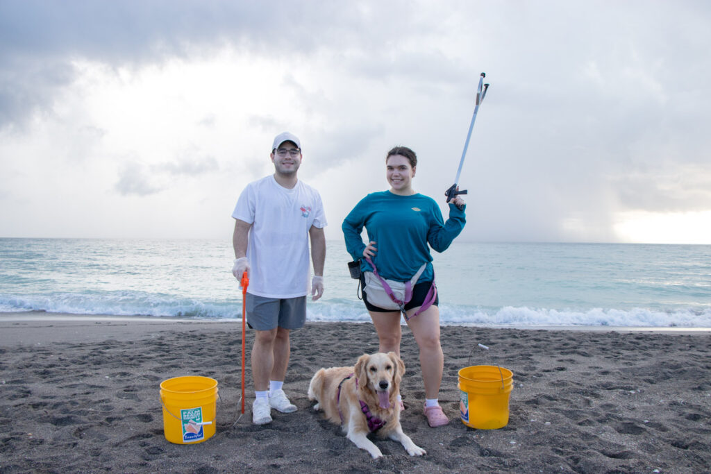 A man, woman, and their dog posing on the beach with cleanup supplies.