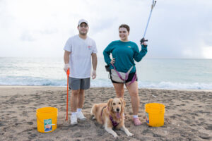 A man, woman, and their dog posing on the beach with cleanup supplies.